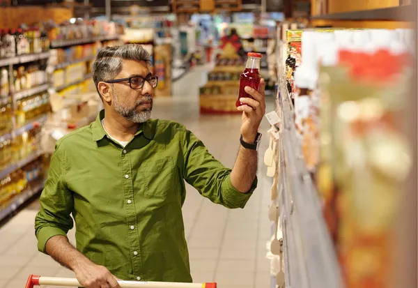 Man shopping in supermarket aisle examining red beverage bottle for influencer product review