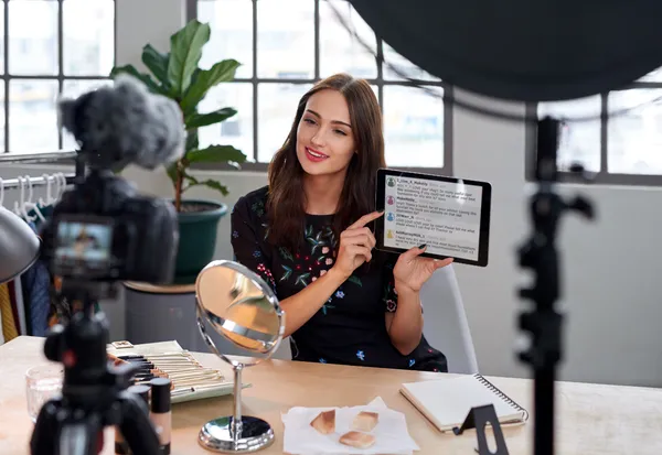 Female creator showing social media comments on tablet while recording video in studio with ring light and cameras