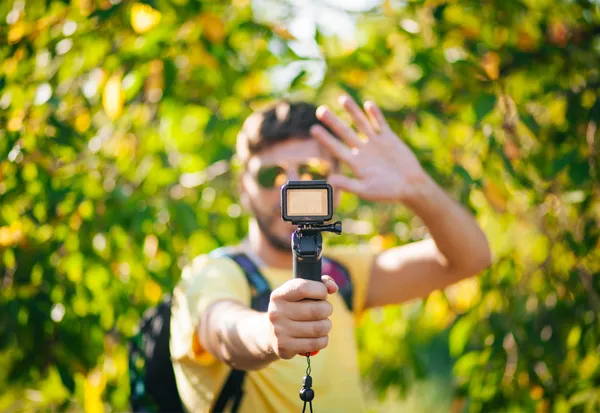 Creator holding action camera on gimbal while filming outdoors in nature for vlog content