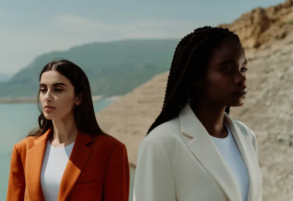Two women in orange and cream blazers pose by water, embodying influencer fashion and lifestyle brand campaign imagery
